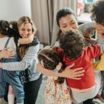 Children and women sharing a heartwarming group hug indoors, expressing love and diversity.